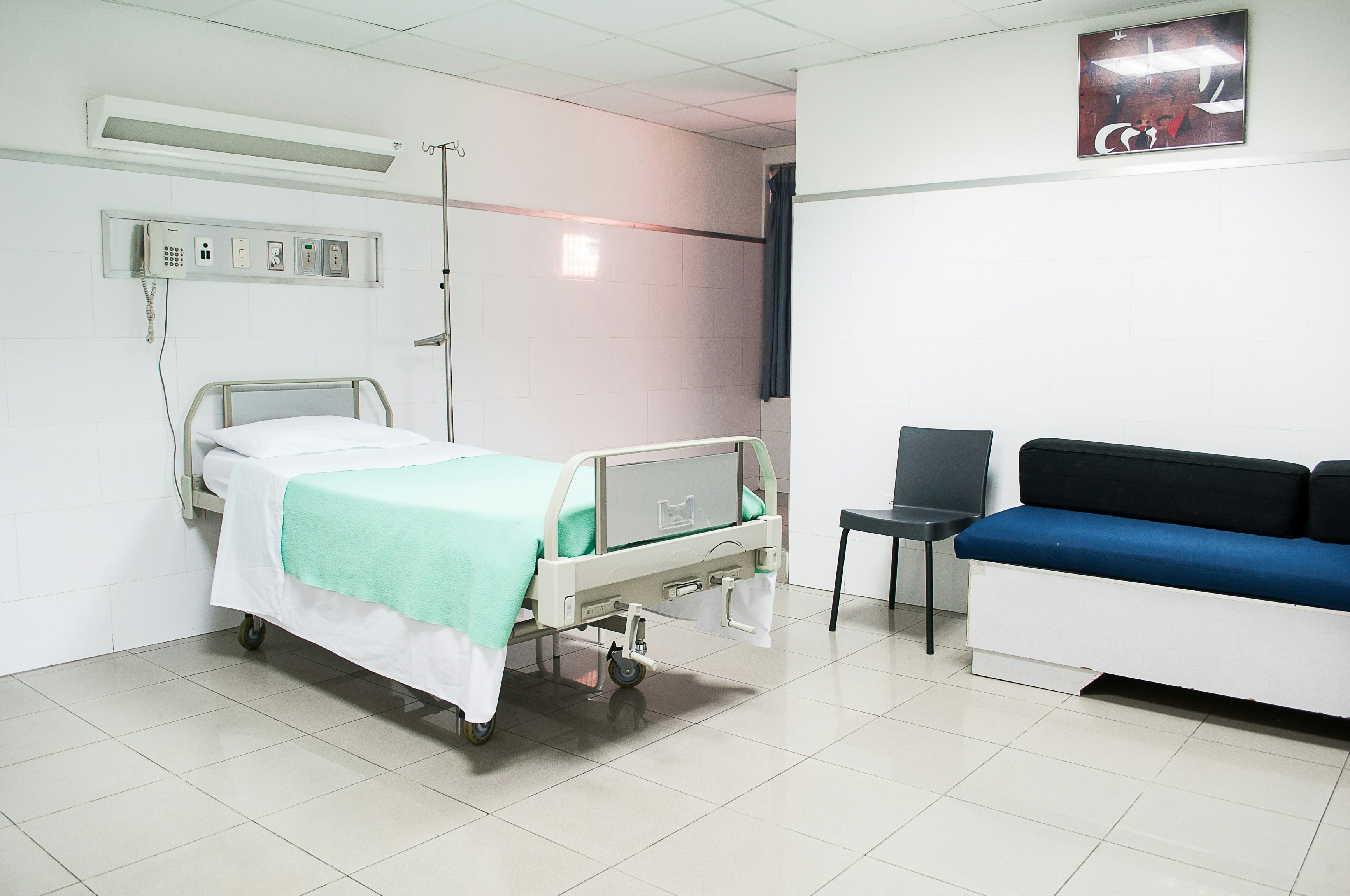 A small hospital bed with green blanket near a blue couch
