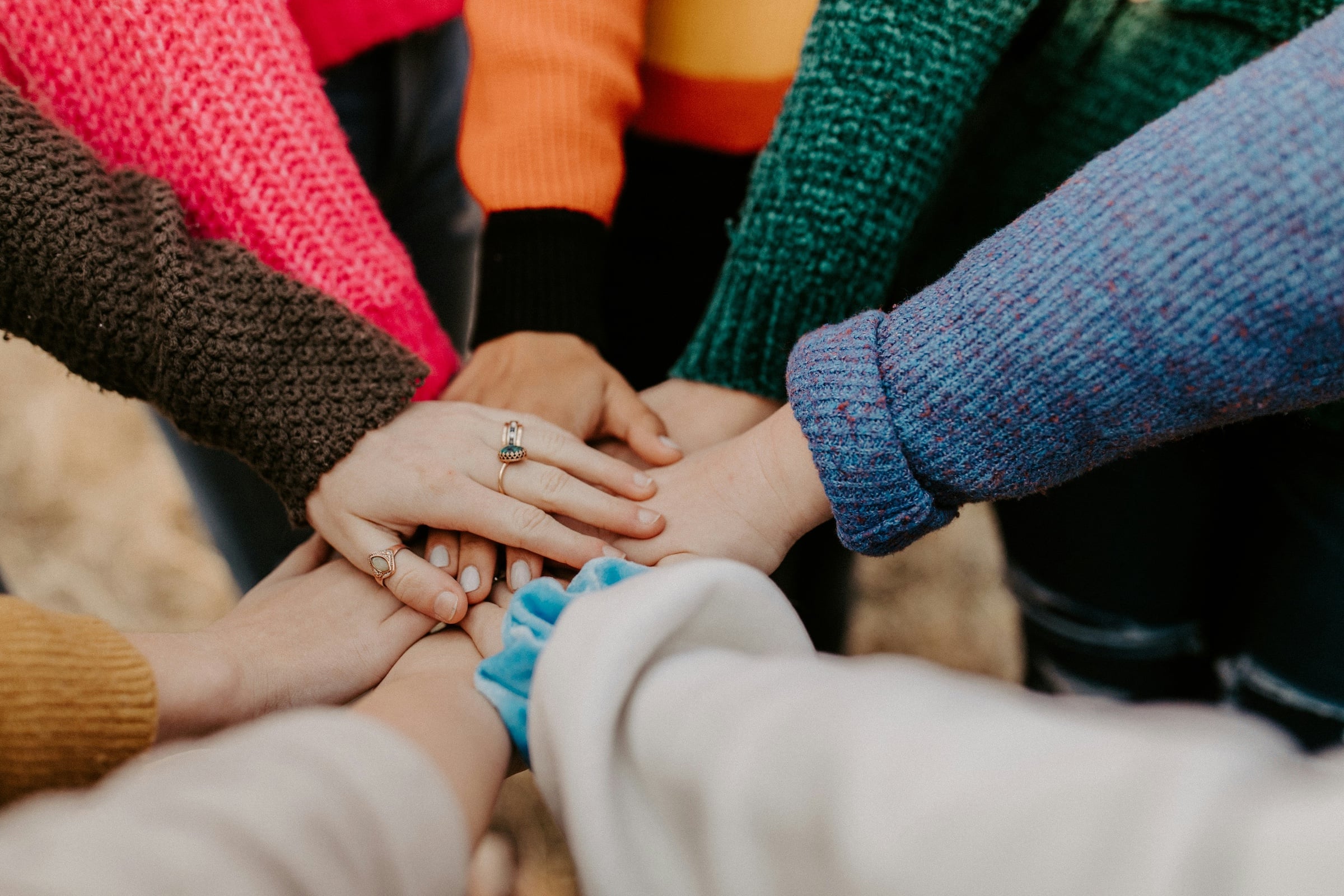Multiple people wearing sweaters putting their hands together in a circle